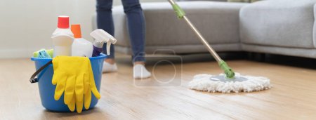 Foto de Trabajadora de servicio ama de llaves feliz fregar piso de la sala de estar por fregona y producto más limpio para limpiar el polvo. - Imagen libre de derechos