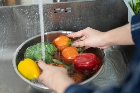Foto de Close up of hands people washing vegetables by tap water at the sink in the kitchen to clean ingredient prepare a fresh salad. - Imagen libre de derechos