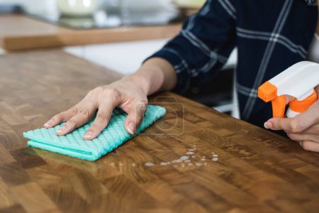 Téléchargez les photos : Femme au foyer nettoyage table en bois par chiffon et solution de nettoyage - en image libre de droit