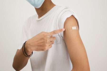 Foto de Happy Asian man showing his arm and bandage after they get a vaccine. - Imagen libre de derechos