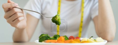 Téléchargez les photos : Unhappy asian women is on dieting time looking at broccoli on the fork. girl do not want to eat vegetables and dislike taste of vegetable. - en image libre de droit