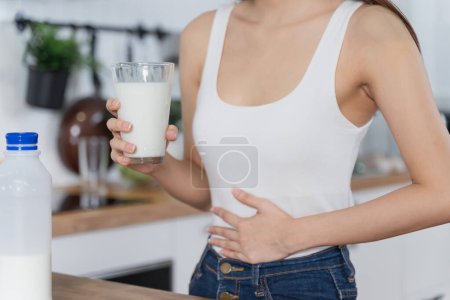 Konzept der Laktoseintoleranz. Frau hält ein Glas Milch und hat Bauchschmerzen.