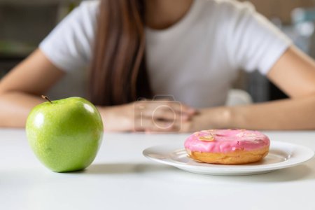 Téléchargez les photos : Femme au régime pour une bonne santé concept. Gros plan femelle comparant beignet préféré et pomme verte pour une bonne santé. - en image libre de droit