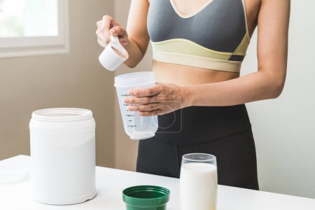 Photo for Young sporty woman pouring protein powder into a cup to make replacement food meal after workout - Royalty Free Image