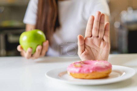 Foto de Mujer en la dieta para un buen concepto de salud. Cerrar hembra usando mano empujar hacia fuera su donut favorito y elegir manzana verde y verduras para una buena salud. - Imagen libre de derechos