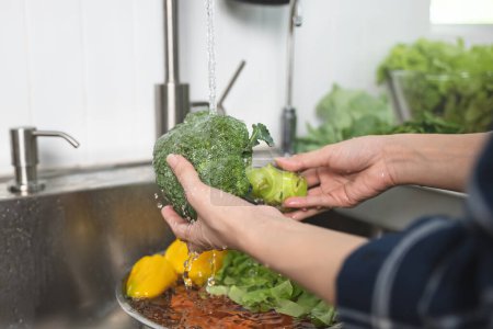 Téléchargez les photos : Close up of hands people washing vegetables by tap water at the sink in the kitchen to clean ingredient prepare a fresh salad. - en image libre de droit