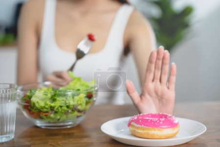 Foto de Mujer en la dieta para un buen concepto de salud. Cerrar hembra usando mano empujar hacia fuera su rosquilla favorita y elegir verduras de ensalada para una buena salud. - Imagen libre de derechos