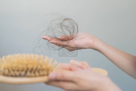 Foto de Hair fall problem concept. Shocked Asian woman looking at many hair lost in her hand and comb. - Imagen libre de derechos