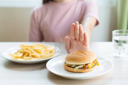 Photo for Woman on dieting for good health concept. Woman doing cross arms sign to refuse junk food or fast food (hamburger and potato fried) that have many fat. - Royalty Free Image