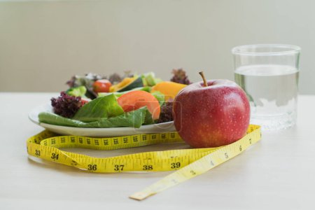 Foto de Good food for good health. Breakfast meal apple and water on the table and measure tape. - Imagen libre de derechos