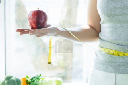 Téléchargez les photos : Aliments biologiques sains pour femme au régime concept. Femme porte une pomme rouge devant une nourriture saine et ayant une mesure sur le bras. - en image libre de droit