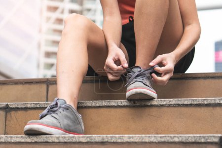 Téléchargez les photos : Close-up hands of woman tying shoelace on the stairs prepare for jogging. - en image libre de droit
