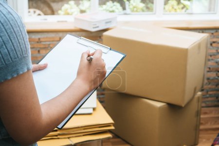 Photo for Happy woman checking stuff in cardboard box before sent to transportation company and movin - Royalty Free Image