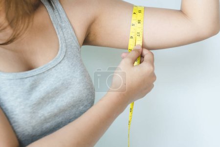 Foto de Mujer midiendo su exceso de grasa del brazo por cinta métrica amarilla sobre fondo aislado. - Imagen libre de derechos