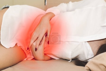 schöne junge asiatische Frau, die auf dem Bett liegt und unter Bauchschmerzen leidet. Weibchen leiden unter Zeit auf dem Bett