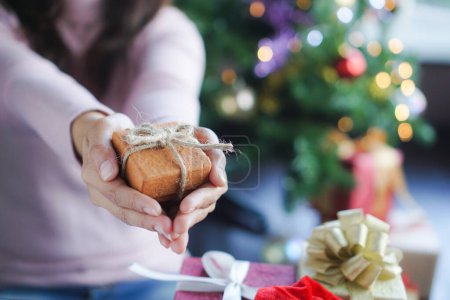 Téléchargez les photos : Mains en gros plan de la femme asiatique tenant boîte cadeau brun minuscule et corde rouge sur les mains se présentant à la famille dans la veille de Noël. - en image libre de droit