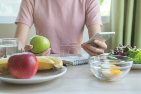 Photo for Dieting and calories control for wellness. Woman using smartphone calculate calories of food in breakfast during dieting for lose weight program and take notes. - Royalty Free Image