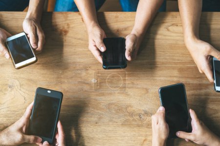 Photo for Group of friends playing app games in mobile phone and online together. Hands are holding smartphone circle on the table. - Royalty Free Image