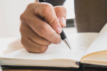 Close up view of hand holding a black luxury pen and writing on notebook diary.