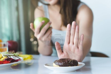 Mujer en la dieta para un buen concepto de salud. Cerrar hembra usando mano empujar hacia fuera su donut favorito y elegir manzana verde y verduras para una buena salud.