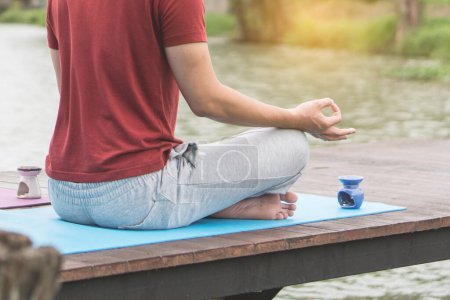 Téléchargez les photos : Homme assis sur le tapis au bord du lac et faisant de la méditation le matin au lac. - en image libre de droit