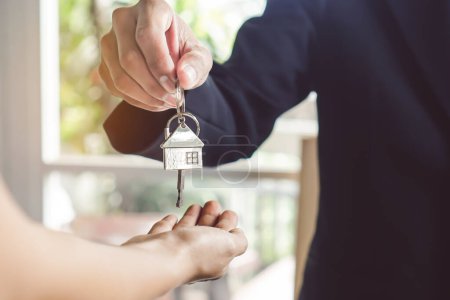 Téléchargez les photos : Vue rapprochée main de l'agent immobilier / propriétaire donnant maison clé à l'acheteur / locataire. - en image libre de droit