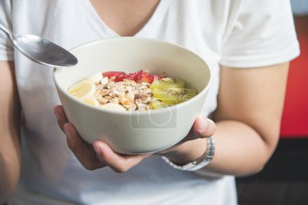 Téléchargez les photos : Eating healthy breakfast concept. Woman holding bowl of cereal and granola and variety fruits and glass of milk on th floor in the morning at home. - en image libre de droit