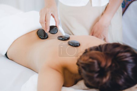 Téléchargez les photos : Spa massage aux pierres chaudes. Belle femme couchée sur le lit se détendre avec spa pierre chaude sur le dos. - en image libre de droit