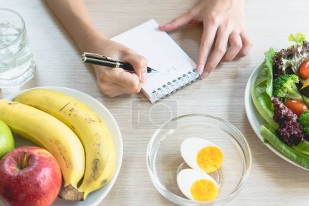 Dieta y control de calorías para el bienestar. Mujer usando smartphone calcular las calorías de los alimentos en el desayuno durante la dieta para bajar de peso programa y tomar notas.