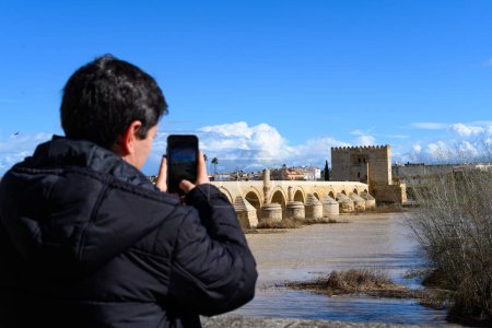 Hombre fotografiando un paisaje del puente romano en Córdoba, España con su teléfono móvil
