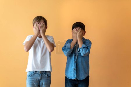 Two standing children covering their faces with their hands.