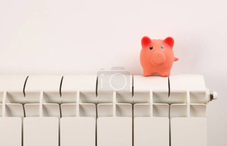 Photo for Piggy bank on radiator. Cold home, Global energy crisis concept. Price for electricity and heating rising. - Royalty Free Image