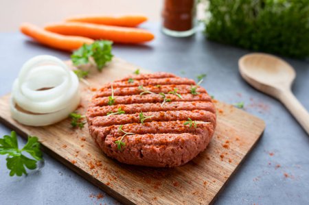 Vegan meatless burger, raw plant-based meat on a cutting board with vegetables, eco-friendly healthy food.