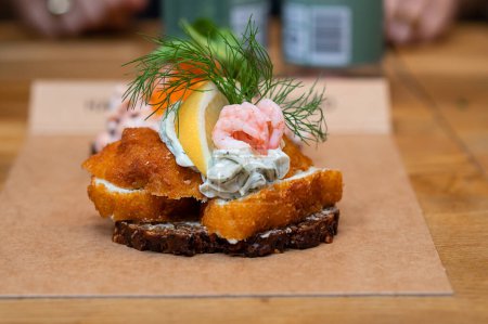 Photo for Danish open sandwich made of rye bread, fried fish and shrimp on a table in a cafe, fast food. - Royalty Free Image