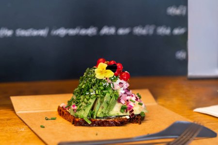Photo for Open sandwich on a table in a cafe, Danish traditional sandwich made of rye bread, avocado, red currants and sauce. - Royalty Free Image