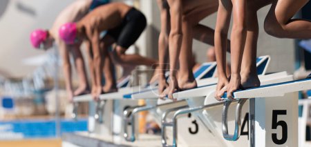 Téléchargez les photos : Enfants adolescents sur les blocs de départ prêts à plonger dans la piscine au début d'une course de natation - en image libre de droit
