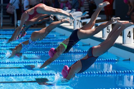Photo for Female swimmers dive off the platform into the swimming pool to swim race - Royalty Free Image