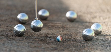 Magnetic pick-up tool for petanque. Petanque balls boules bowls on closeup on sand gravel court background, lifting the ball with a magnet