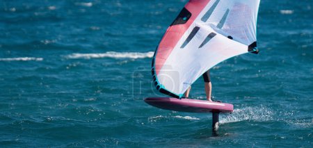 Photo for A man is wing foiling using handheld inflatable wings and hydrofoil surfboards in a blue ocean, rider on a wind wing board, surf the waves - Royalty Free Image
