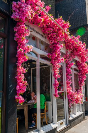 Foto de LONDRES, Reino Unido - 24 de mayo de 2023: Una espectacular exhibición floral decora la ventana del restaurante La Mia Mamma en Chelsea durante la exposición anual de arte floral Chelsea in Bloom en Londres - Imagen libre de derechos