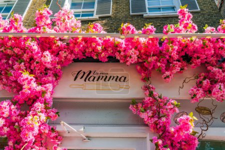 Foto de LONDRES, Reino Unido - 24 de mayo de 2023: Una espectacular exhibición floral decora la ventana del restaurante La Mia Mamma en Chelsea durante la exposición anual de arte floral Chelsea in Bloom en Londres - Imagen libre de derechos