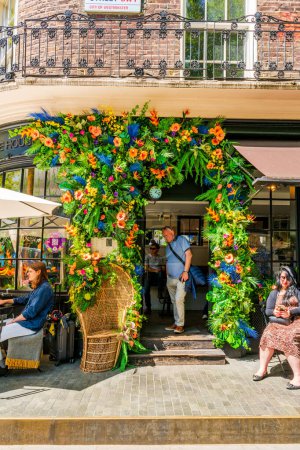 Foto de LONDRES, Reino Unido - 26 de mayo de 2023: Una espectacular exhibición floral decora la ventana de una cafetería en Chelsea durante la exposición anual de arte floral Chelsea in Bloom en Londres - Imagen libre de derechos