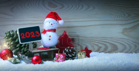 Photo for Christmas snowman with red scarf and santa claus hat , isolated on wood background. Happy New Year 2023 - Royalty Free Image