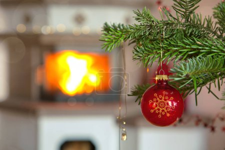 Photo for Christmas tree branch with red ball and blur burning fireplace background. - Royalty Free Image