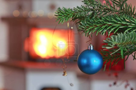 Foto de Rama de árbol de Navidad con bola azul y fondo de chimenea borrosa. - Imagen libre de derechos