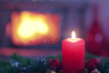Foto de Vela de Adviento rojo ardiente en un interior cálido con chimenea. - Imagen libre de derechos