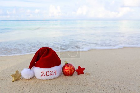 Foto de Feliz Navidad sombrero y decoraciones en la arena blanca del Caribe.Año Nuevo 2024 fondo - Imagen libre de derechos