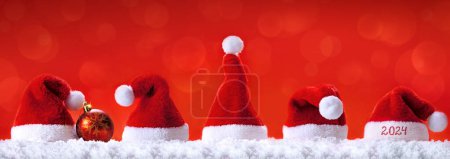 Photo for Santa hats on white snow isolated on red background. Happy new Year 2024 . - Royalty Free Image