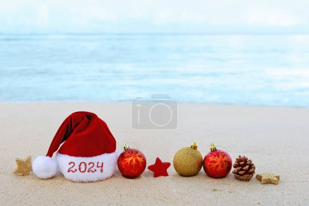 Photo for Merry Christmas hat on the white Caribbean sand. New Year 2024 background - Royalty Free Image