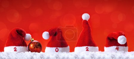Photo for Santa hats on white snow isolated on red background. Happy new Year 2024 . - Royalty Free Image